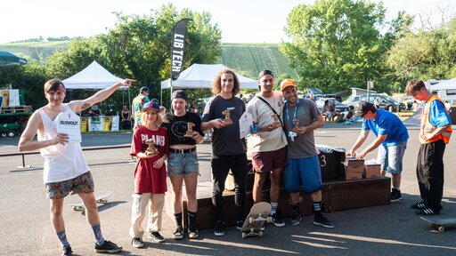 Siegerehrung SnR-ConFest 2023. Mehrere junge Menschen stehen auf einer Straße, mit einem Skateboard und halten einen Preis in der Hand.